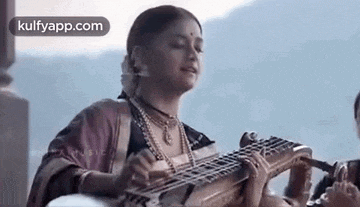 a woman is playing a musical instrument while standing in front of a mountain .