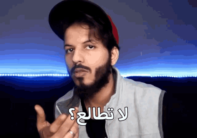 a man with a beard is wearing a hat and a vest with arabic writing