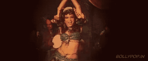 a woman is dancing in a dark room with a man playing a drum in the background .