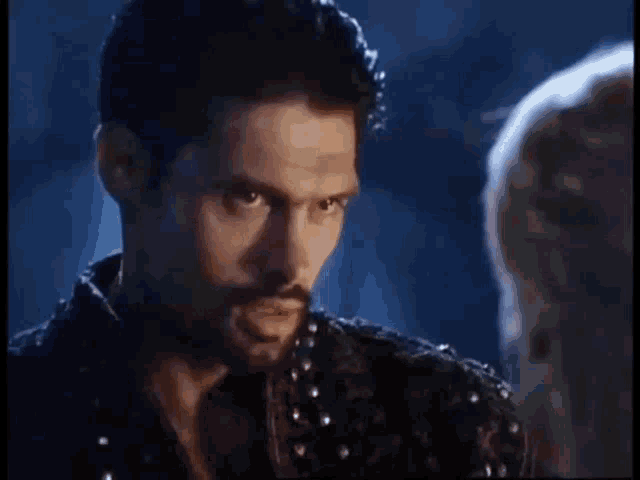 a man with a beard is looking at another man in the dark .