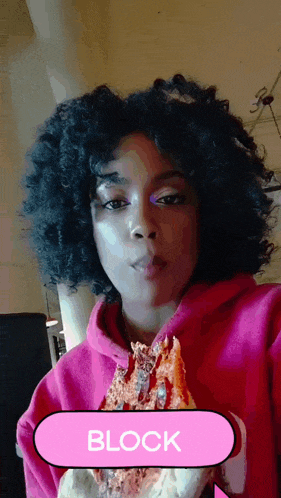 a woman in a pink hoodie is holding a slice of pizza and the word block is above her head