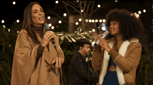 two women singing into microphones with a man playing a keyboard in the background