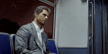 a man in a suit sits in a blue seat on a train
