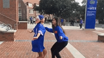 two women are dancing on a brick sidewalk in front of a gate 18 sign .