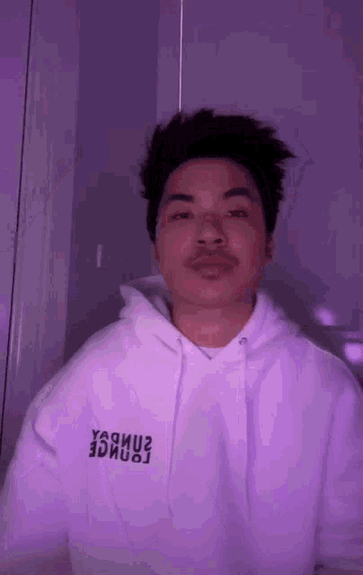 a man wearing a white hoodie with a purple background is standing in front of a purple wall .
