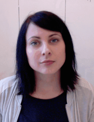 a woman with dark hair and blue eyes is wearing a black shirt and a grey jacket
