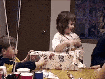 a little girl sitting at a table holding a box that says saturday