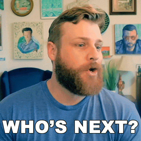 a man with a beard wearing a blue shirt says " who 's next "