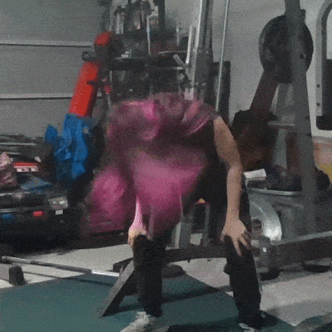 a woman with pink hair is sitting on a bench in a gym with her head on a barbell .