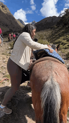 a woman pushes a brown horse on a dirt path