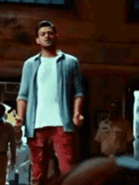 a man in a blue shirt and red pants is standing in front of a group of people in a room .