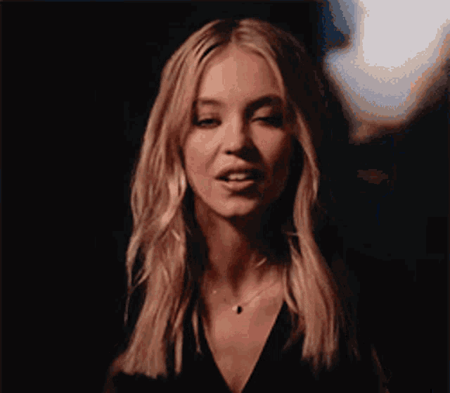 a woman with blonde hair is wearing a black top and a necklace