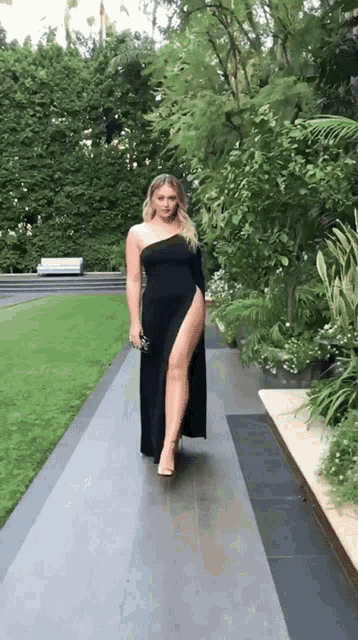 a woman in a long black dress is walking down a sidewalk .