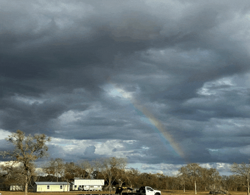 a white truck is parked in front of a house with a rainbow in the sky above it