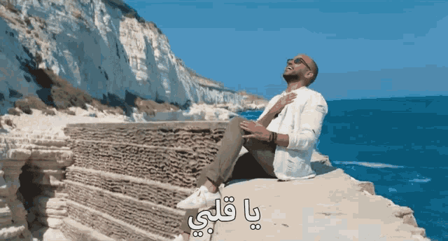 a man sits on a cliff overlooking the ocean with arabic writing on the bottom