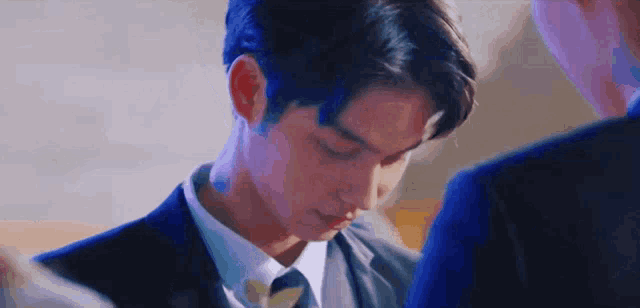 a man in a suit and tie is looking down at something while standing next to another man .