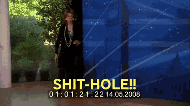 a woman stands in front of a blue wall that says shit-hole on it