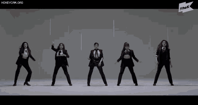 a group of women in suits are dancing in front of a sign that says the k