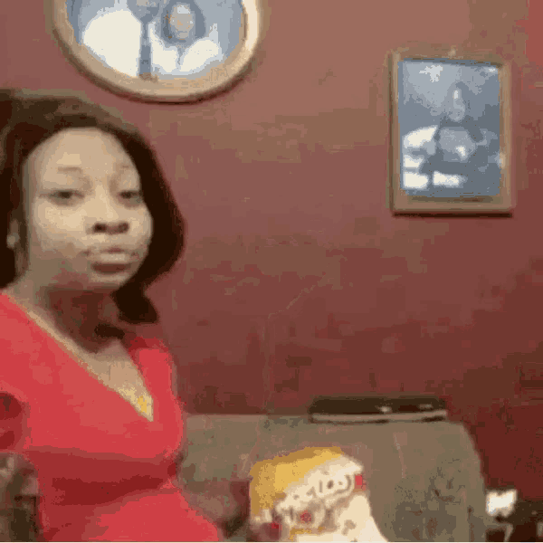 a woman in a red shirt is sitting on a couch in front of a picture of a man and woman .