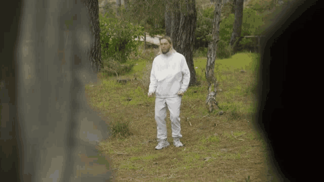 a man in a white sweatshirt stands in a forest