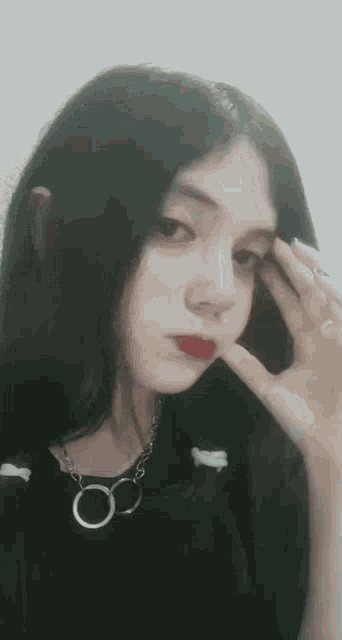 a girl with long black hair and red lipstick is wearing a black shirt and a chain necklace .
