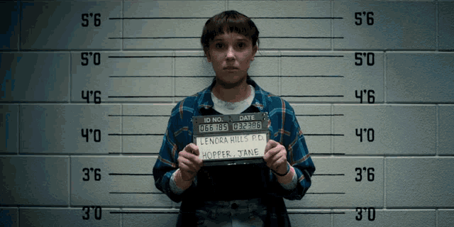 a woman in a blue plaid shirt is holding a mugshot that says lenora hills r.d. hopper jane