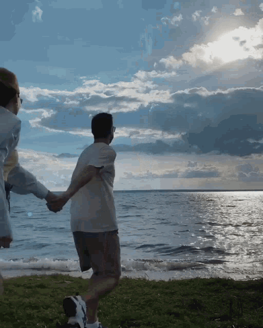 a man and a woman holding hands on a beach with the sun shining through the clouds