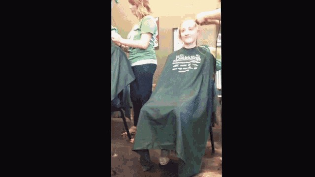 a girl is getting her hair cut at a barber shop with a green cape that says ' barber ' on it