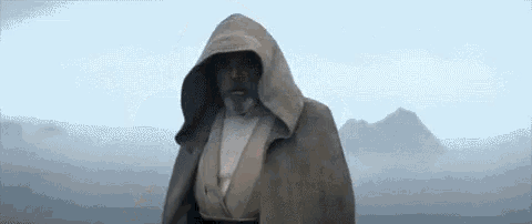 a man with a beard and a hooded cape is standing in a field .