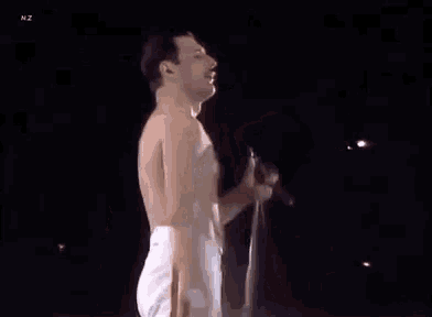 a shirtless freddie mercury is singing into a microphone on stage .