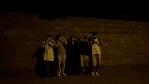 a group of people standing in front of a wall with one wearing a shirt that says ' a ' on it