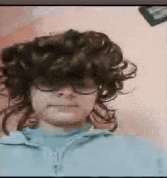 a woman with curly hair and glasses is wearing a blue shirt and a blue sweater .