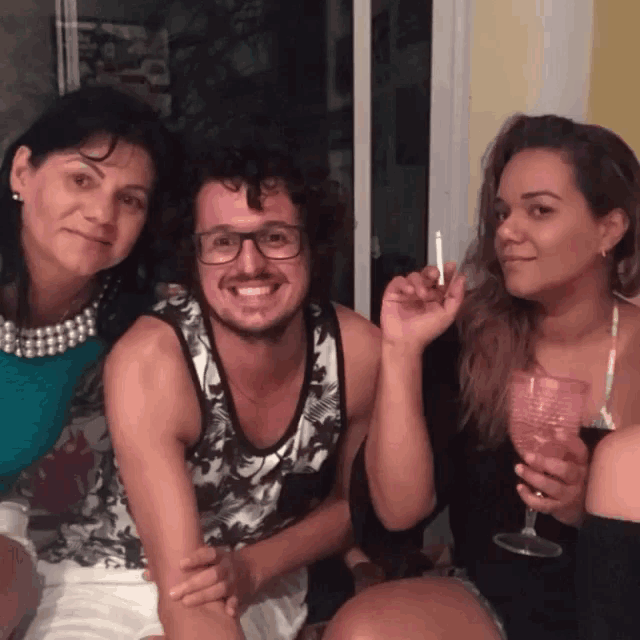 a man smoking a cigarette while two women hold wine glasses