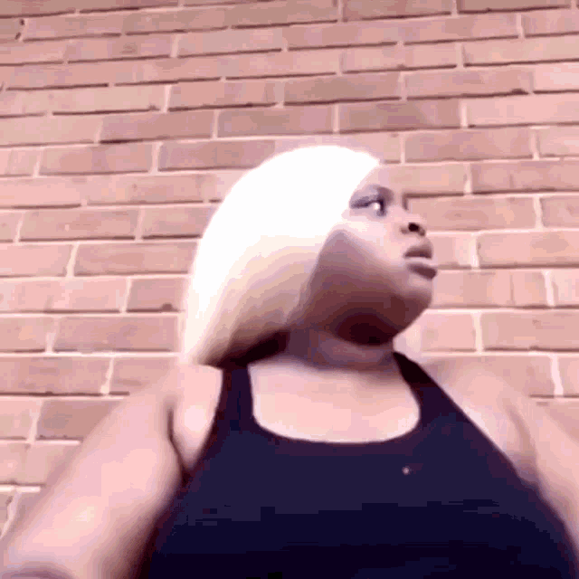 a woman with blonde hair wearing a black tank top is standing in front of a brick wall