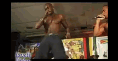 a shirtless man is singing into a microphone in front of a sign that says " loud video "