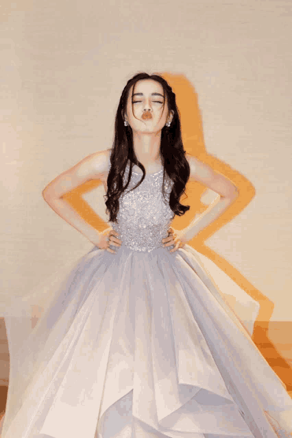 a woman in a long gray dress blowing a kiss