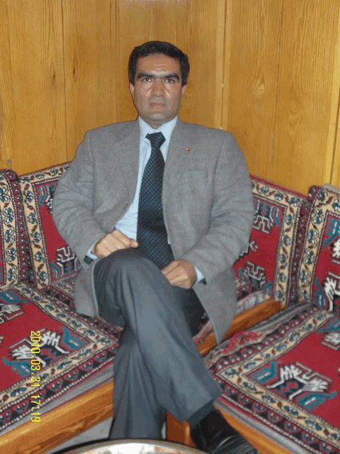 a man in a suit and tie sits on a couch with a photo taken on january 27th 2009