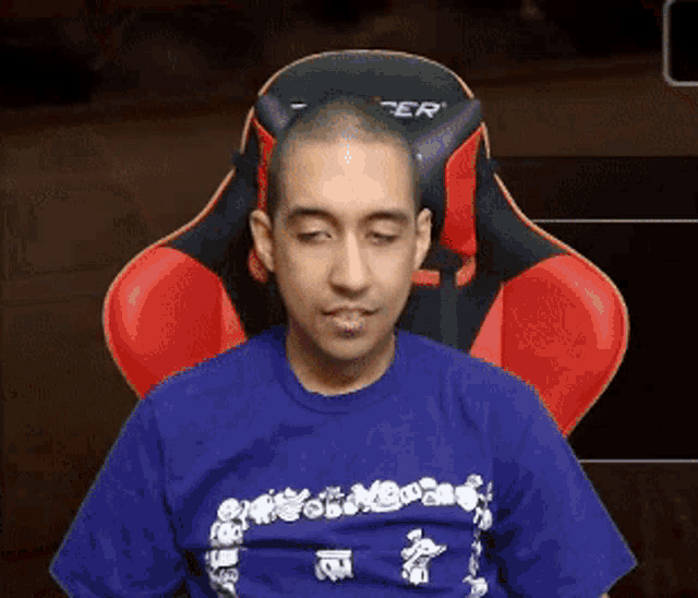 a man in a blue shirt is sitting in a red and black chair with the word per on it