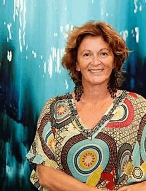 a woman in a colorful shirt is smiling in front of a blue wall .