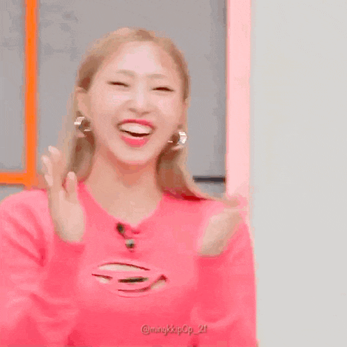 a woman in a pink sweater is smiling in front of a yellow circle with korean writing on it