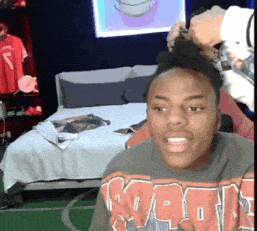a man wearing a sweatshirt that says ' nba ' on it is sitting in a bedroom next to a bed .