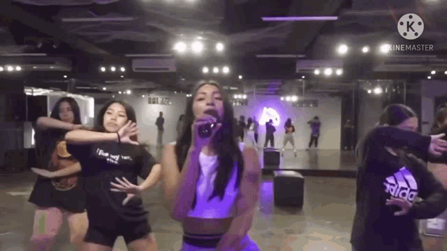 a woman is singing into a microphone in a dance studio with other women .
