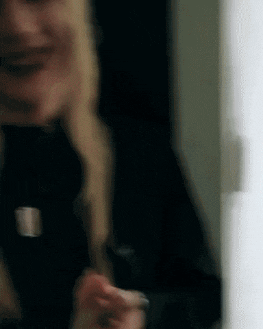 a woman in a black jacket is smiling and holding a cell phone in her hand .