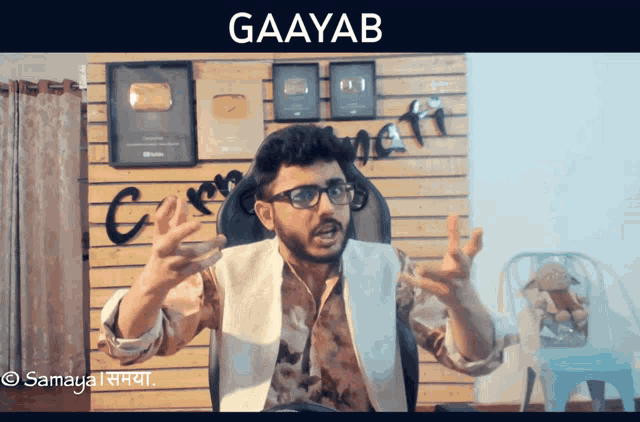 a man with glasses is sitting in front of a wall that says " gaayab "