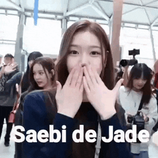 a girl is covering her mouth with her hands while standing in front of a crowd .