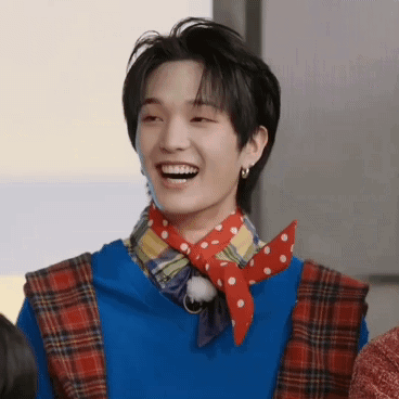 a young man wearing a blue sweater and a red scarf is smiling and laughing .