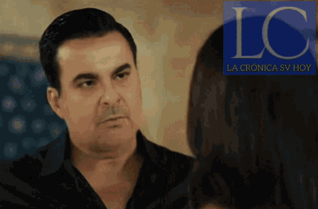 a man in a black shirt is looking at a woman with a lc la cronica sv hoy logo behind him