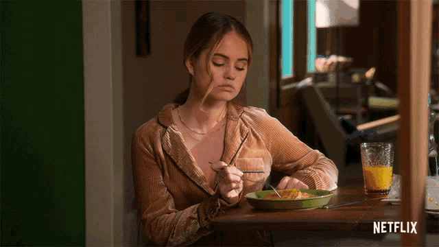 a woman sits at a table with a plate of food and a glass of orange juice with netflix written on the bottom