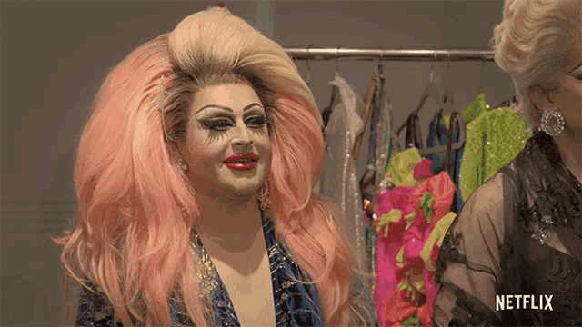 a drag queen with pink hair is standing in front of a netflix logo