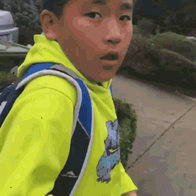 a young boy wearing a yellow hoodie and a blue backpack looks surprised
